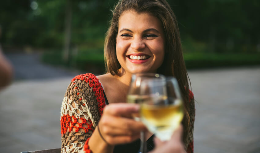A happy woman clicking her wine glass to another person’s glass