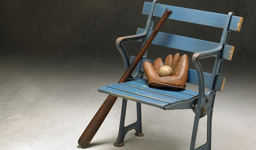 An old baseball glove, ball, and bat on a blue vintage stadium chair