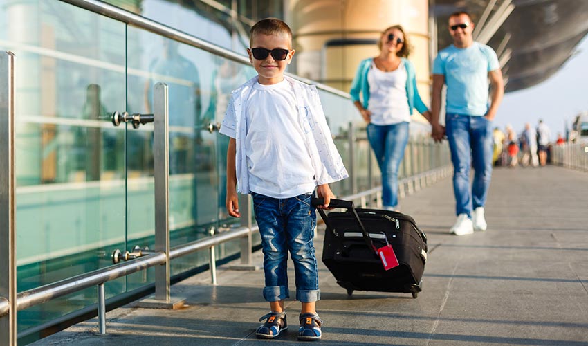 Little boy pulling his suitcase in an airport in front of his parents