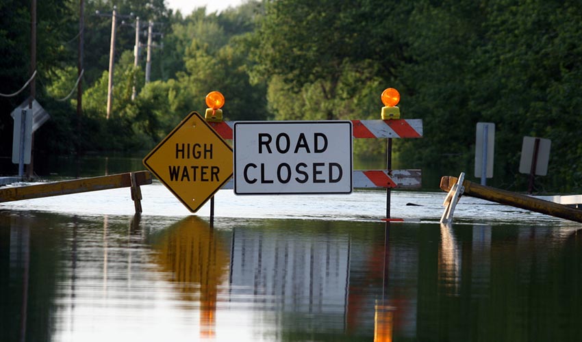 A flooded road with a road closed sign