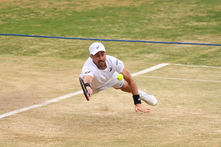 A male tennis player dives for the ball with his racquet extended outward.  