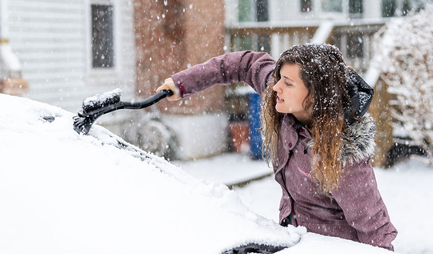 A woman scraping ice and snow off of her car