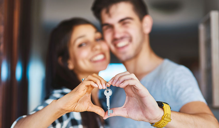 A couple holding their new home keys in a heart shape with their hands