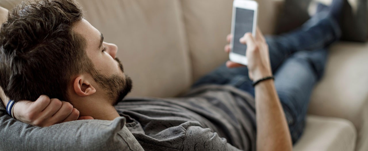 man lying down on couch with his phone