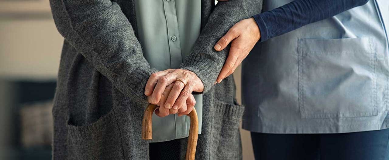 nurse assisting elderly woman with cane
